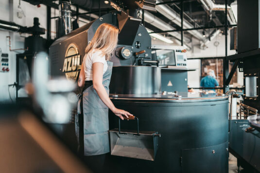 azul-kaffee-roesereiAmDeich Eine weiblich gelesene Person, die an der Rösttrommel in der Rösterei am Deich steht
